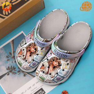 Taylor Swift Fearless Crocs shown with box on blue surface, featuring detailed stamp artwork and portrait.